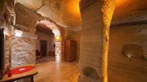 A stone-walled interior with wooden flooring, a table with a red placemat, and a wooden cabinet. - Göreme Cave Lodge (Nevsehir)