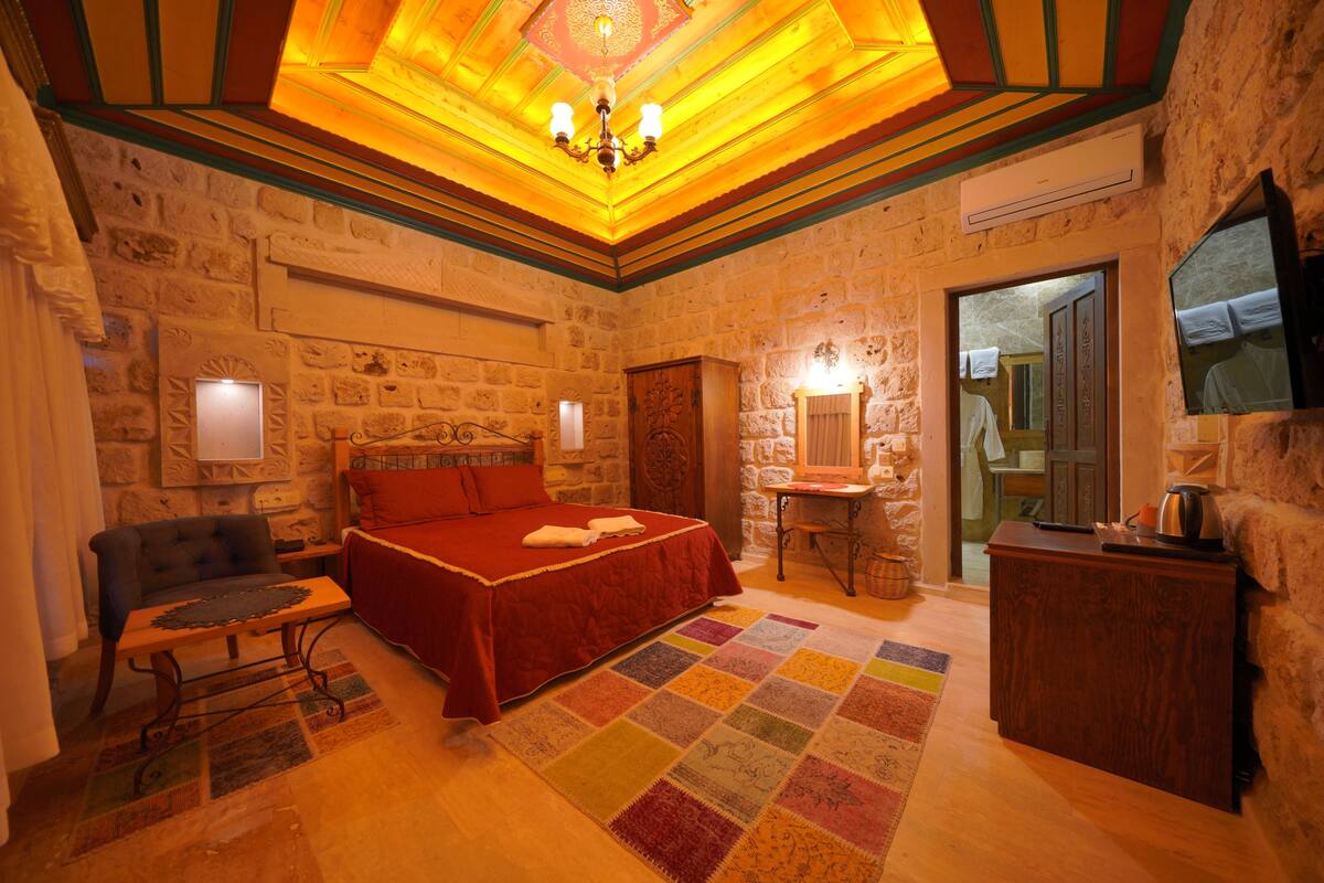 A cozy room with a bed, a chair, a table, and a mirror.