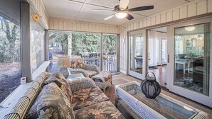 A covered patio with wicker furniture, a ceiling fan, and a glass door leading to an outdoor area.