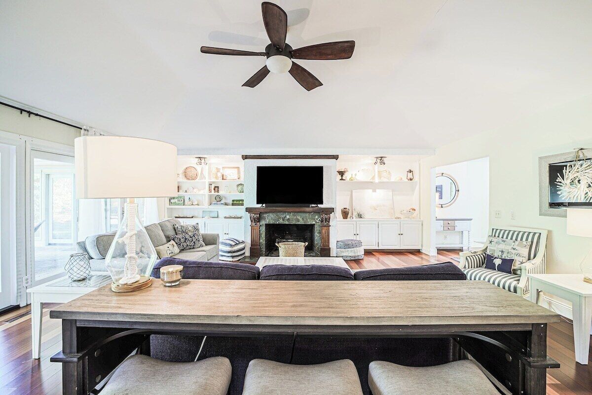 A modern living room with a large wooden dining table, a fireplace, and a ceiling fan.