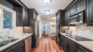 A narrow kitchen with dark wood cabinets, a stainless steel refrigerator, and a microwave on the countertop.