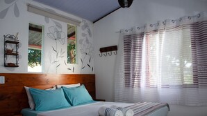 Una cama bien tendida con una manta a rayas, cabecera de madera y ventana con vistas a la vegetación.