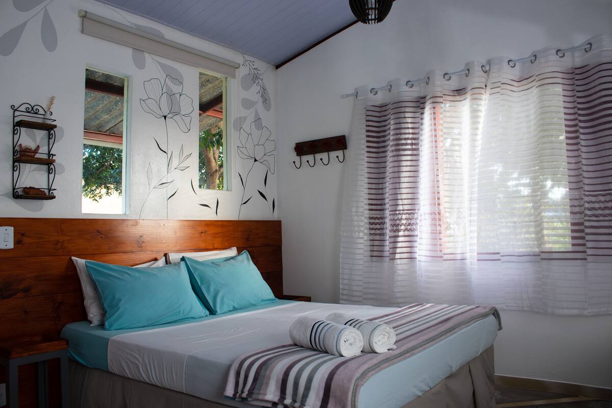 A neatly made bed with a striped blanket, a wooden headboard, and a window with a view of greenery.
