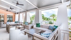 Ein Außenbereich mit Loungemöbeln, Deckenventilatoren und großen Fenstern mit Blick auf Palmen und einen Pool.