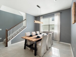 A dining area with a wooden table, white chairs, and a hanging light fixture.