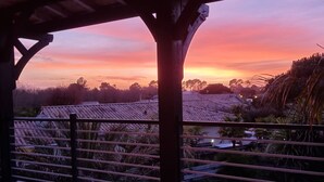 En træterrasse med udsigt til solnedgang over et boligområde.