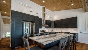 A modern kitchen with dark cabinetry, a stainless steel refrigerator, a marble island, and wooden flooring. - Stunning Ocean Front Condo (Oceans 6) (Pine Knoll Shores)