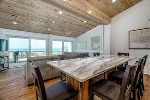 Enjoy ocean views from the room's large windows, featuring a dining table, sofa, and framed maps.