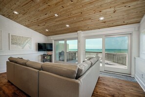 Relax in this stylish living area with a sofa, flat-screen TV, and sliding glass door leading to a balcony with ocean views.