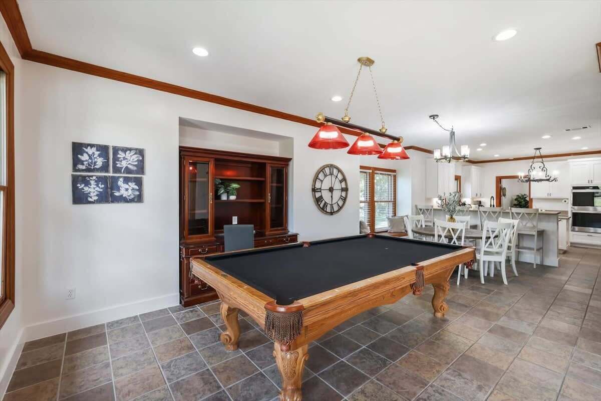 Een pooltafel in een ruime kamer met een keukenhoek, houten kasten en een eethoek.