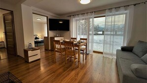 A modern living room with a dining area, a flat-screen TV mounted on the wall, and a large window with a view of a snowy landscape. - Pokoje Gościnne Magnas (Poronin)