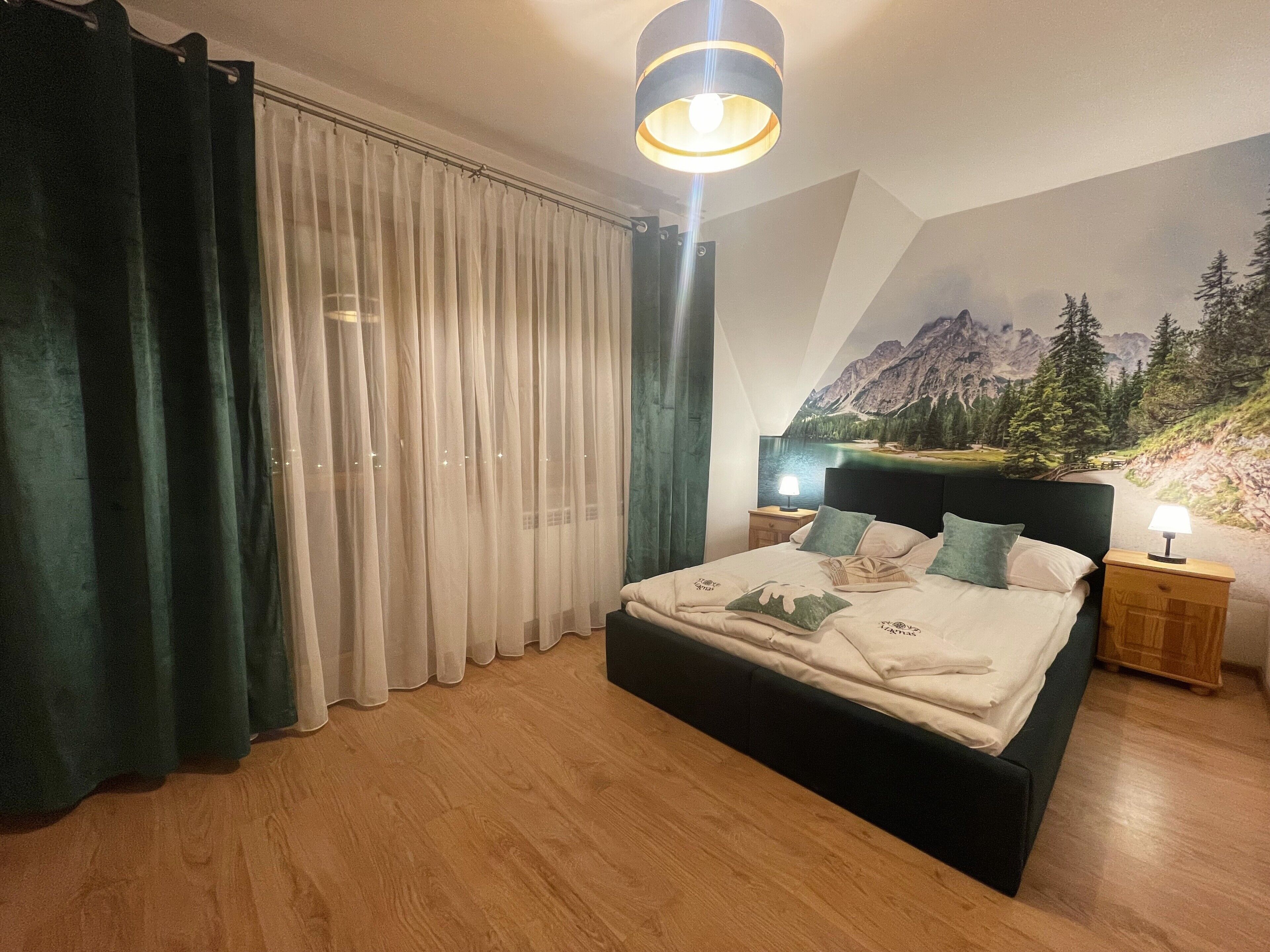 A bedroom with a bed, a nightstand, a lamp, a curtain, and a mural on the wall.