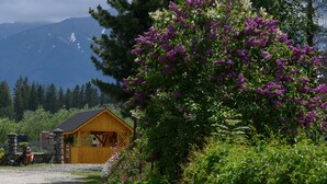 A rustic wooden cabin with a stone foundation, surrounded by lush greenery and purple flowers. - Pokoje Gościnne Magnas (Poronin)