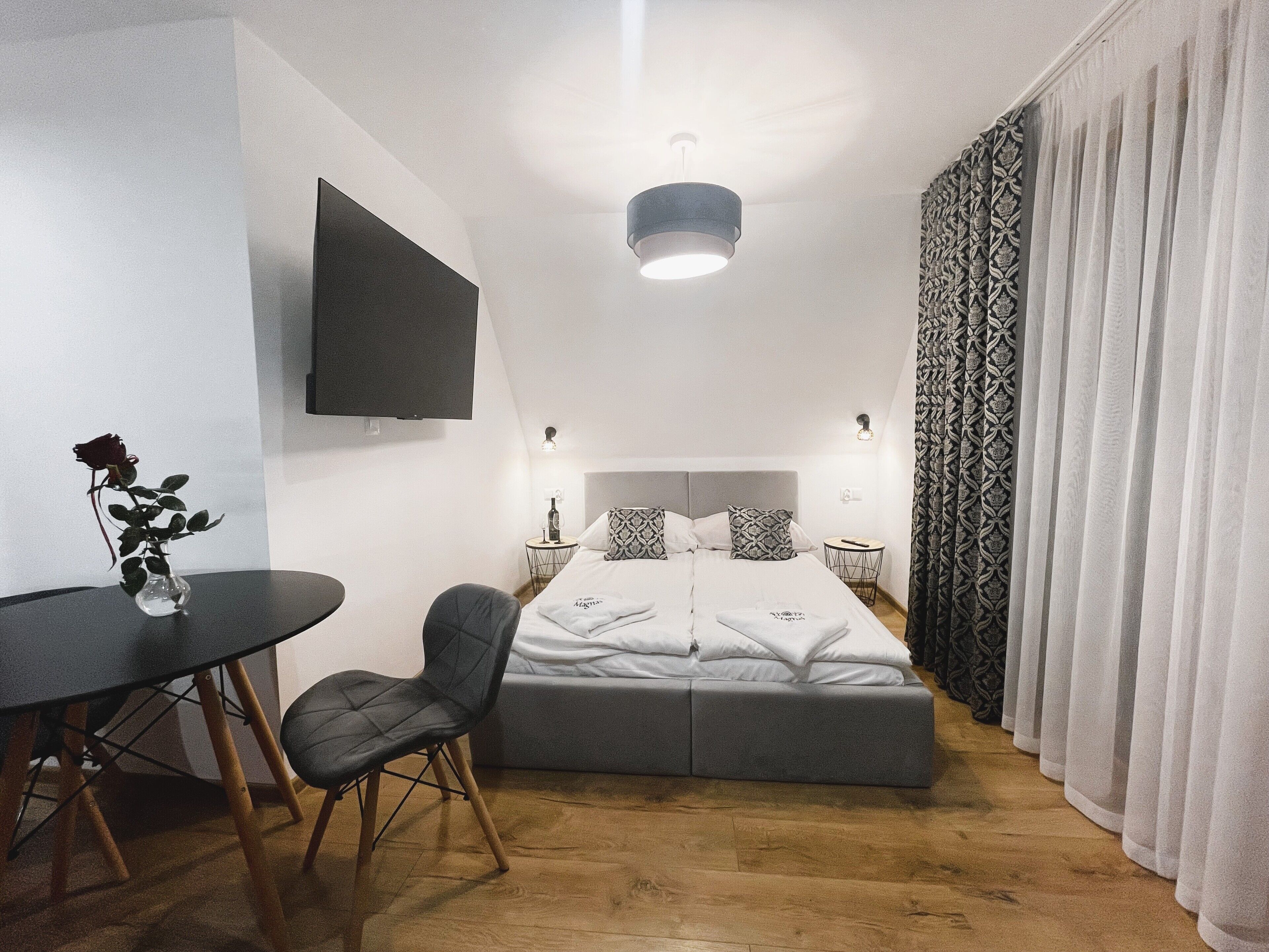Una habitación de hotel moderna con cama, escritorio, silla, televisor y un florero con una rosa.