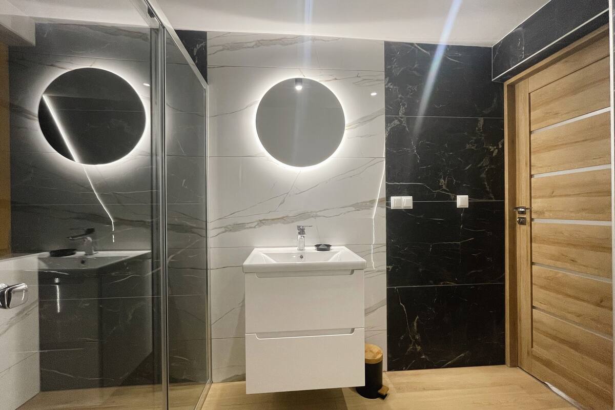 A modern bathroom with two sinks, a mirror, and a wooden door.