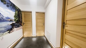 A hallway with two wooden doors, a tiled floor, and a mural of a coastal scene on the left wall. - Pokoje Gościnne Magnas (Poronin)