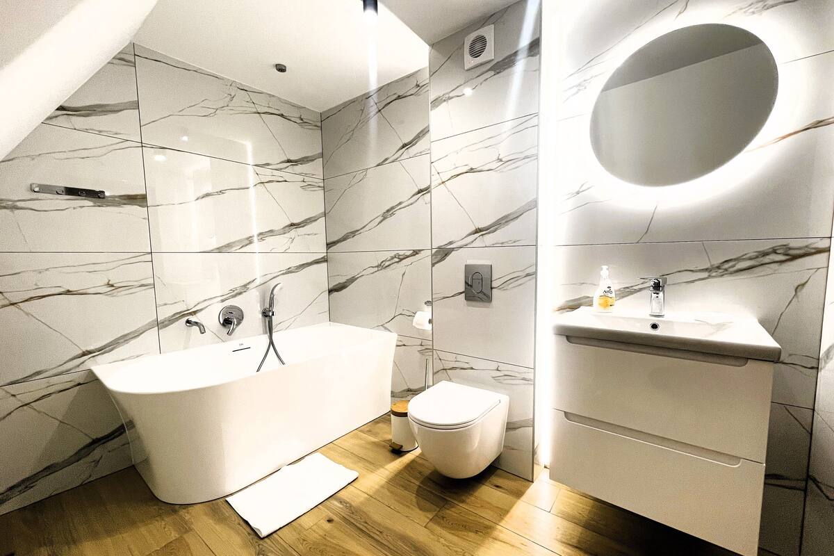 A modern bathroom with a freestanding bathtub, a toilet, and a sink with a circular mirror.