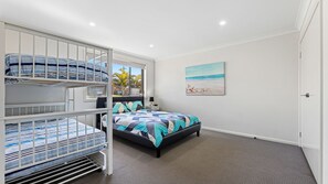 Ein Zimmer mit Etagenbetten, einem Bett mit gemustertem Bettbezug, einem Nachttisch und einem Strandbild an der Wand.