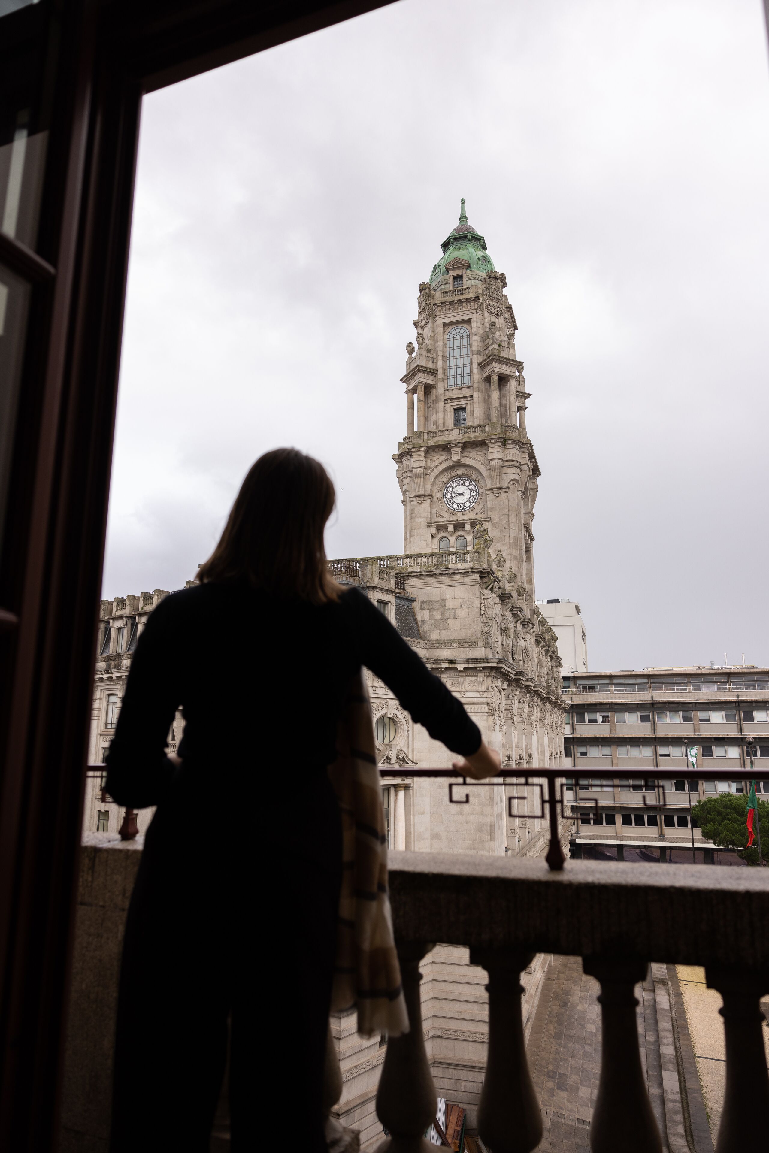 A person standing by a window overlooking a historic building with a clock tower.