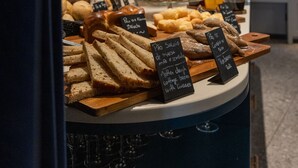 A bakery display with various breads and pastries, including a loaf of bread and a sign indicating a coffee and croissant combo. - Axis Porto Club Aliados (Porto)