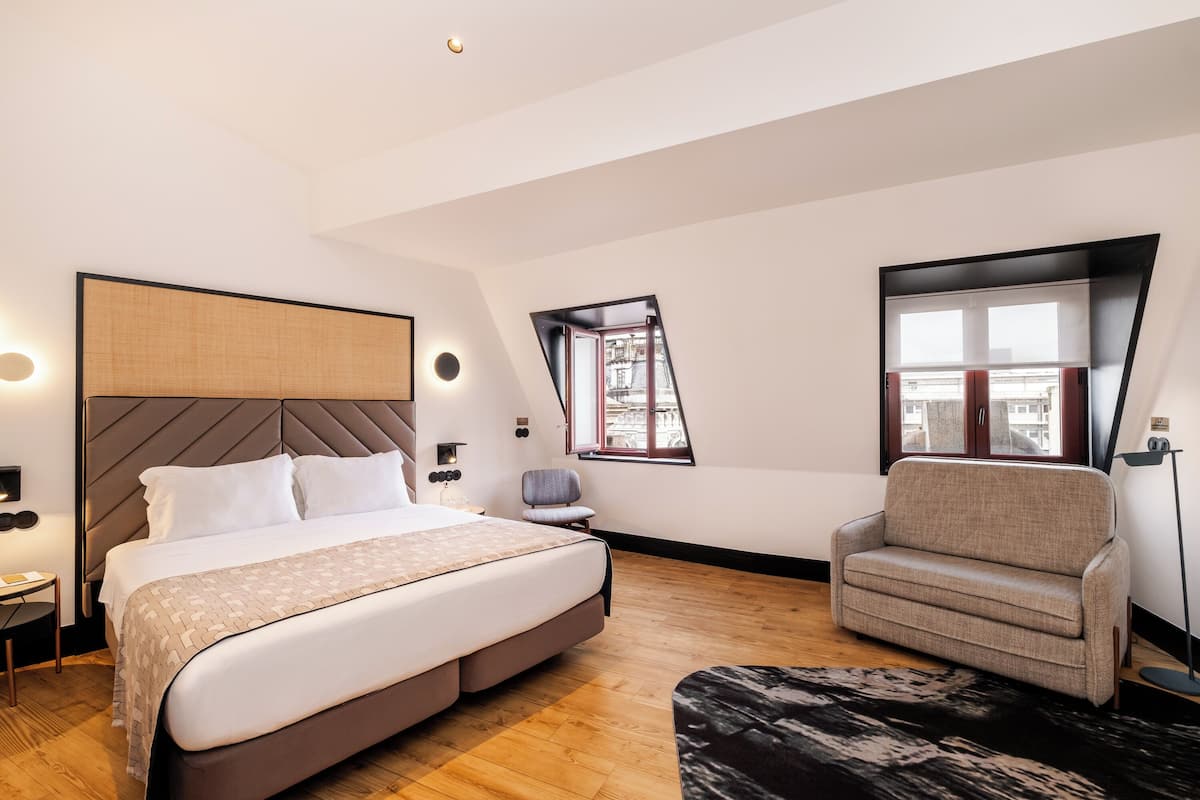 A modern bedroom with a large bed, a sofa, a chair, and a window with a view.