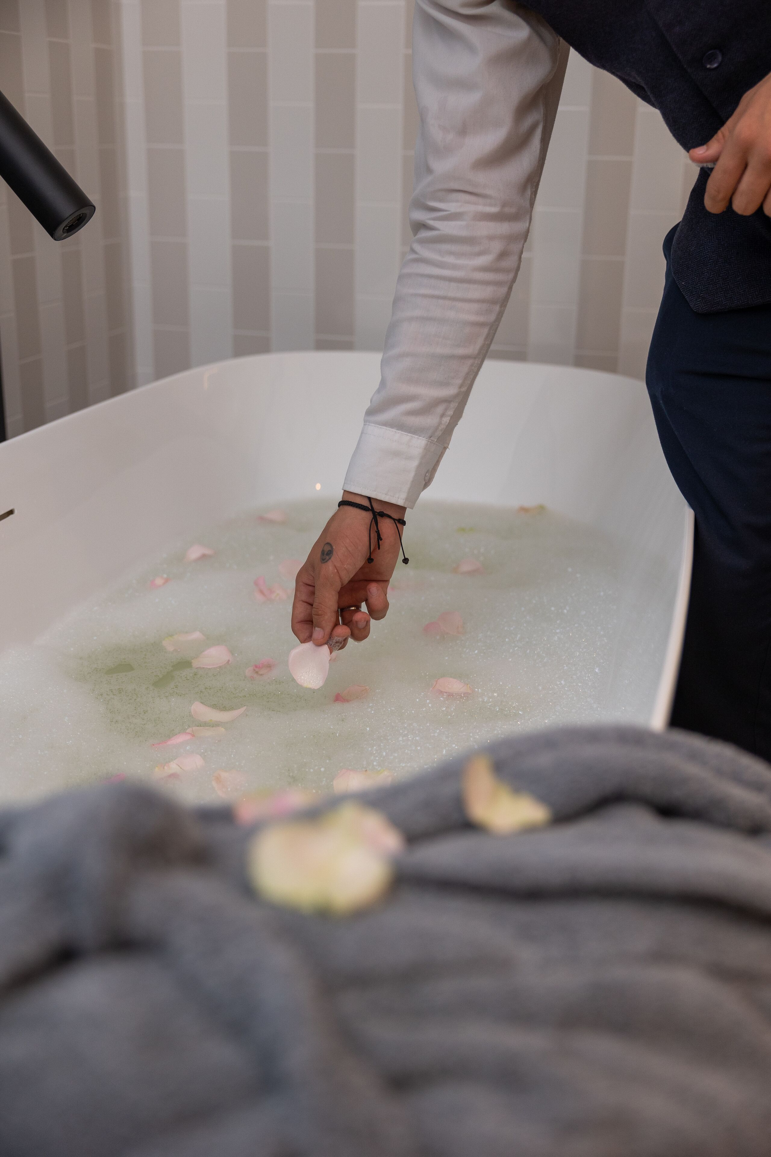 Eine Person in einem weißen Hemd gibt Rosenblätter in eine mit Wasser gefüllte Badewanne.