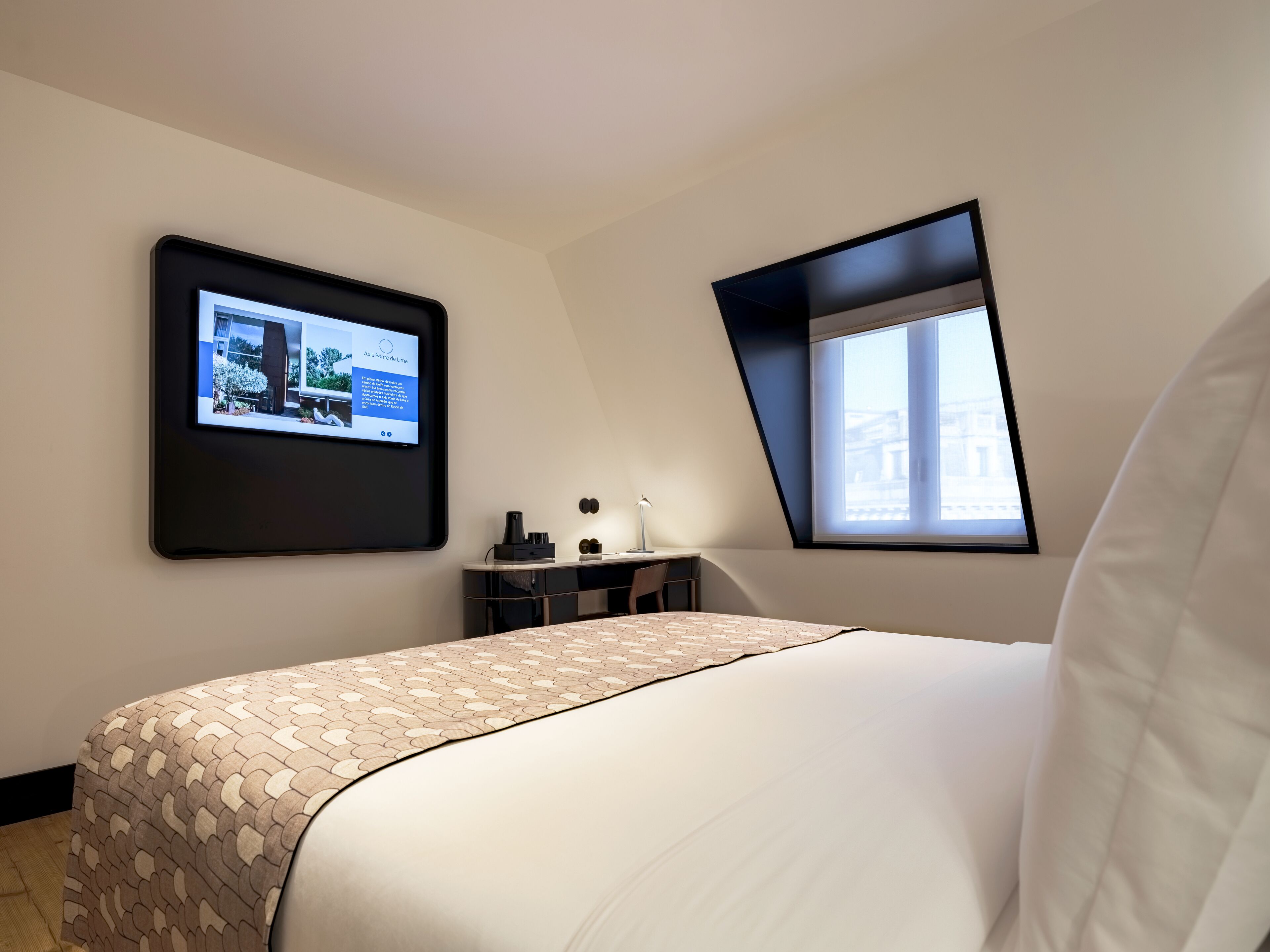 A modern bedroom with a bed, a desk, and a TV mounted on the wall.