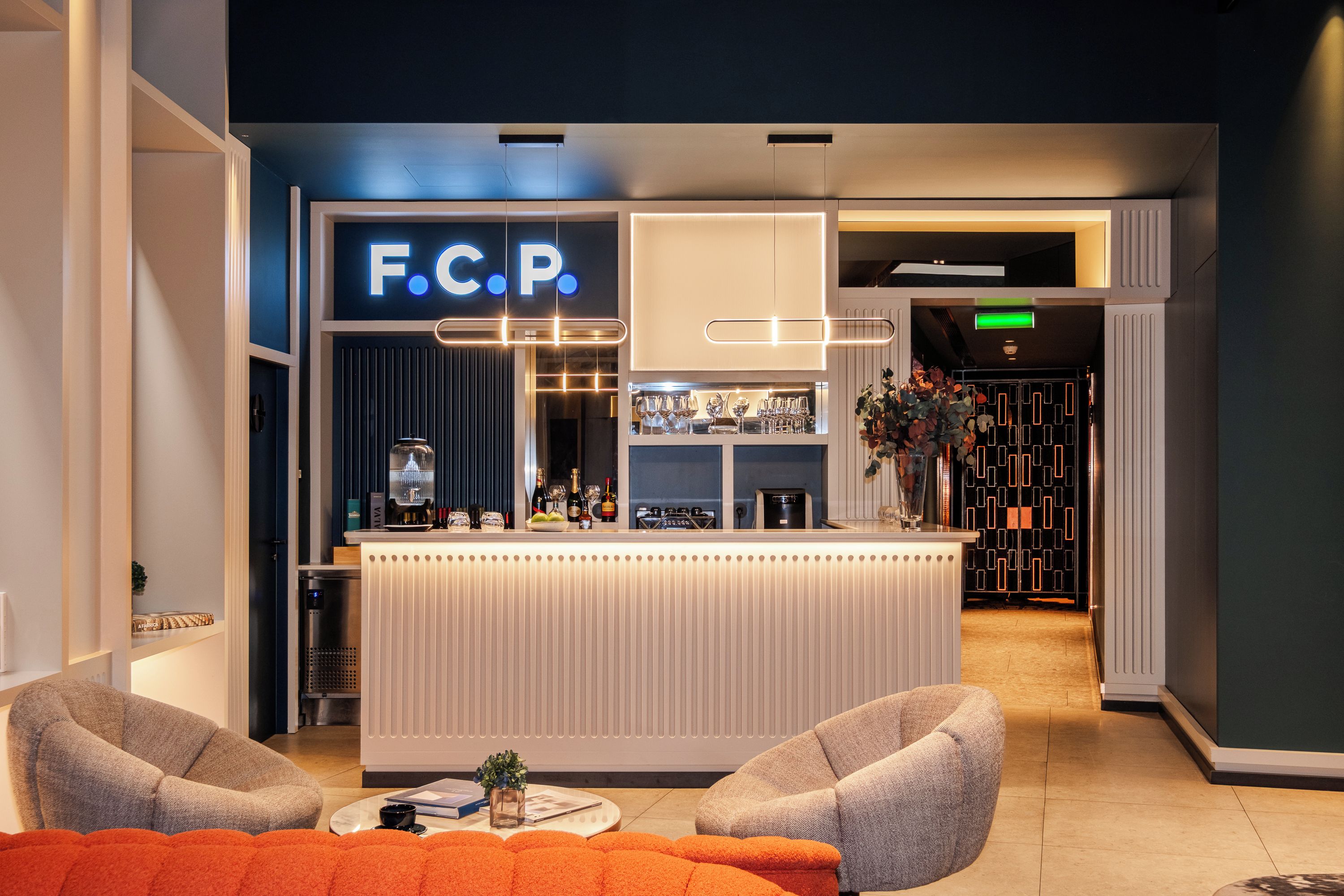 A modern bar area with a neon sign, bar stools, and a seating area with a sofa and armchairs.