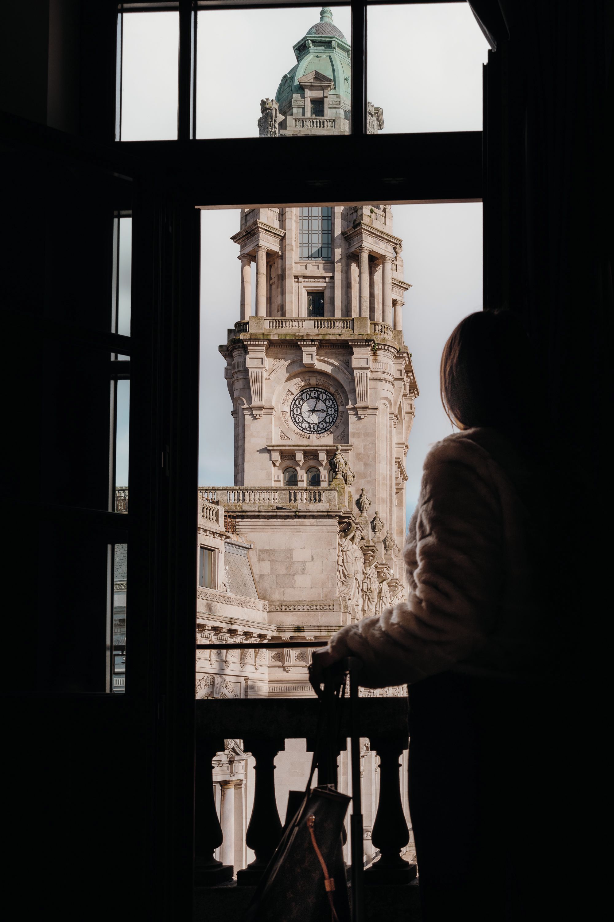 A person looking out of a window at a historic building with a clock tower.
