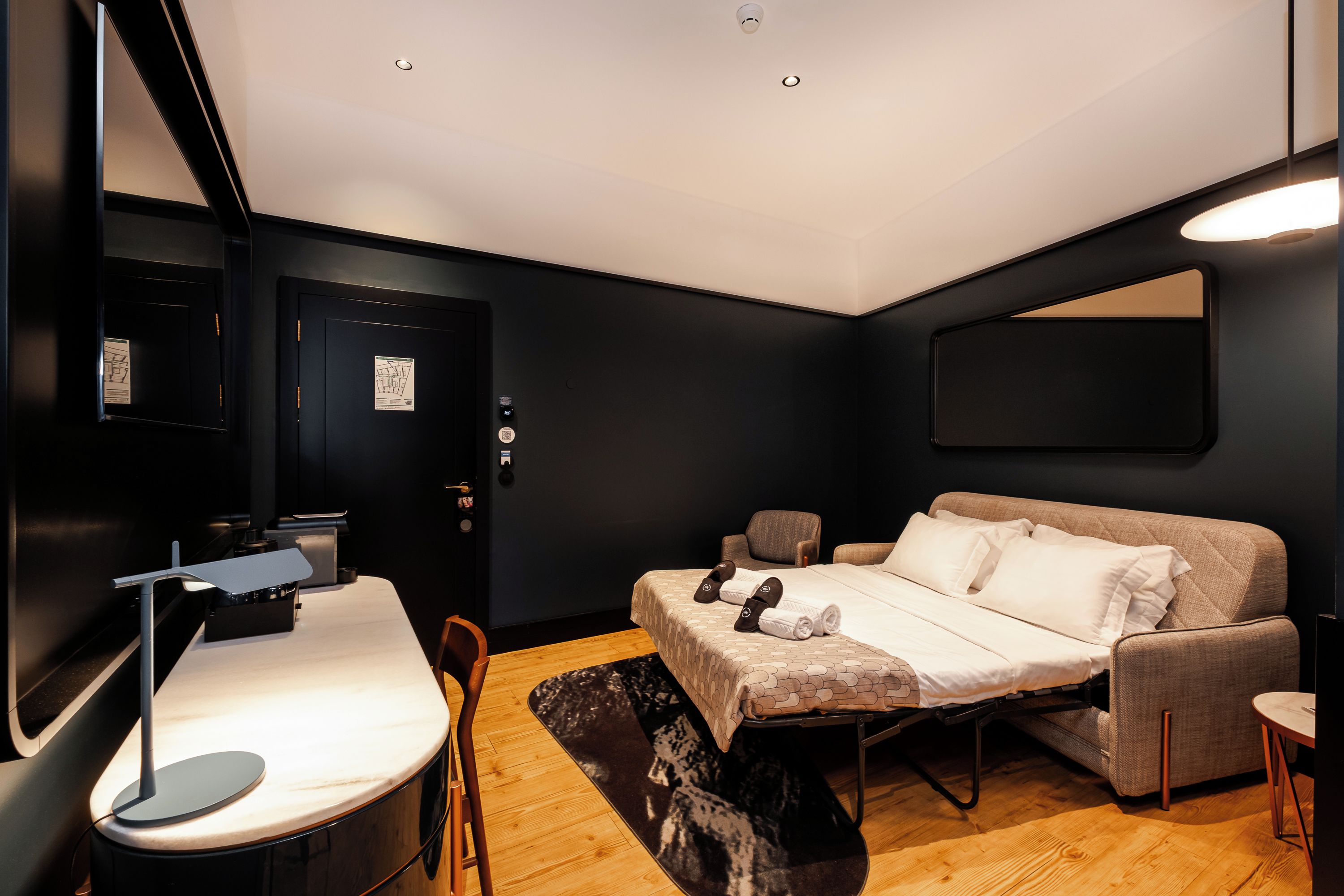 A modern hotel room with a bed, a desk, a chair, and a small table.