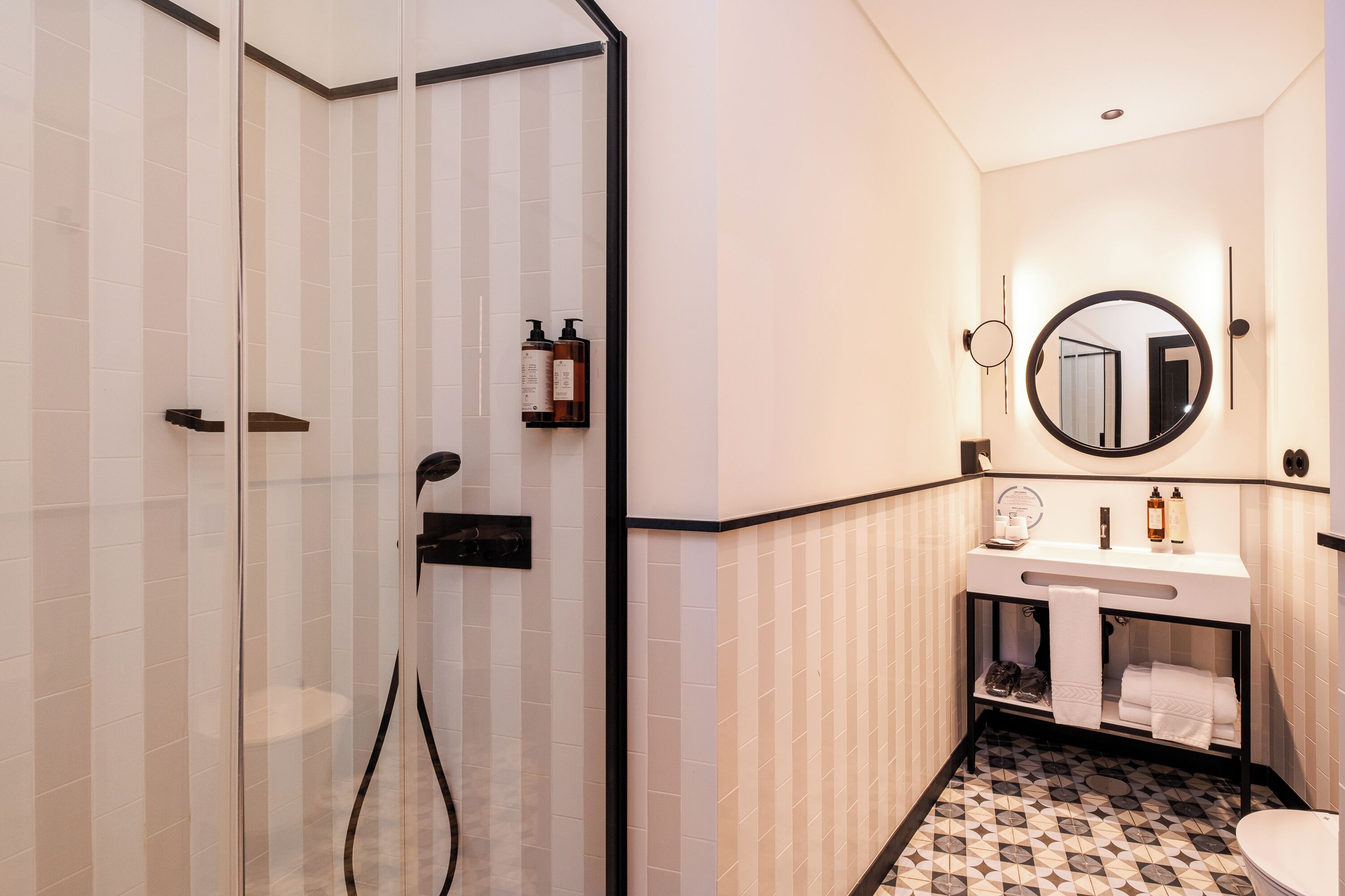 A modern bathroom with a glass-enclosed shower, a vanity with a mirror, and a tiled floor.