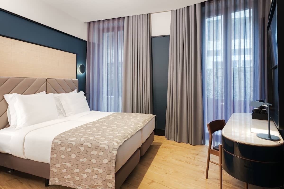 A modern hotel room with a bed, a desk, and a chair.