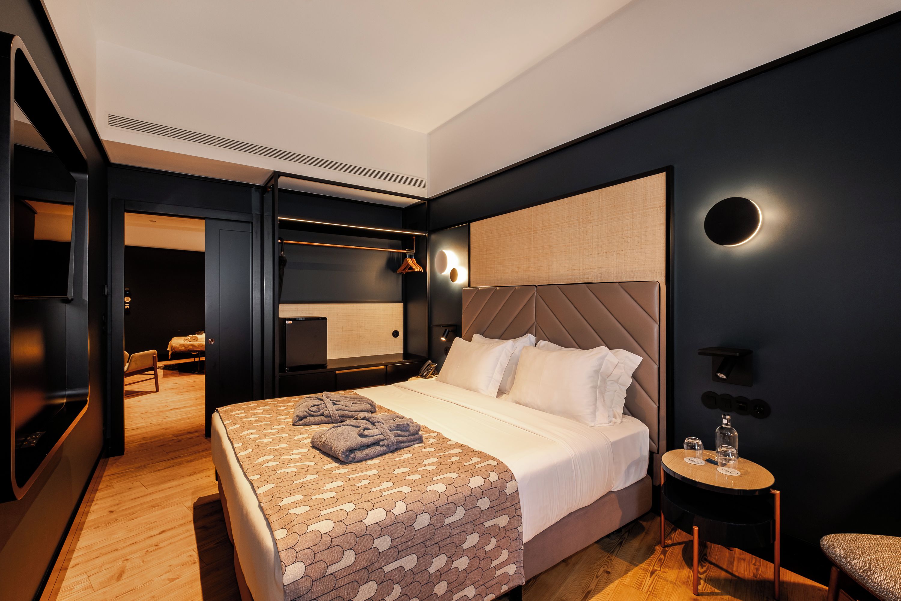 Een moderne hotelkamer met een groot bed, nachtkastje en een klein rond tafeltje met glazen en een fles.