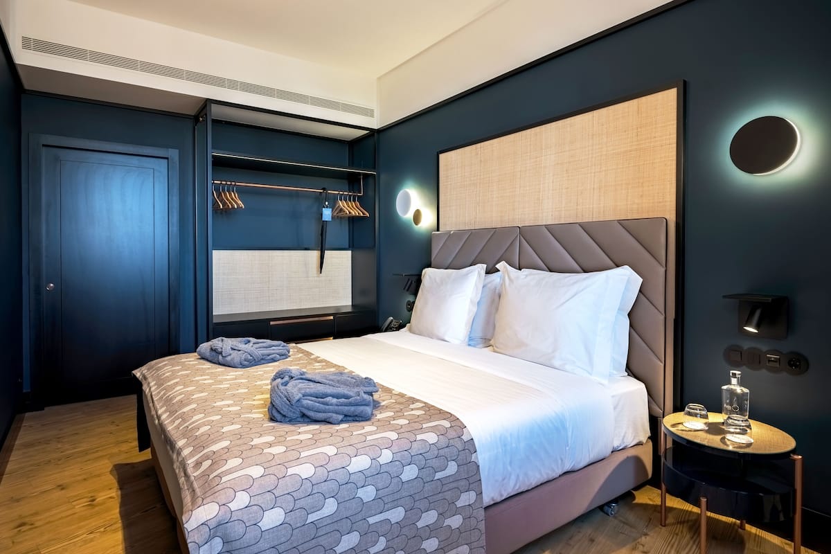 A modern hotel room with a large bed, a bedside table with a lamp, and a wall-mounted TV.