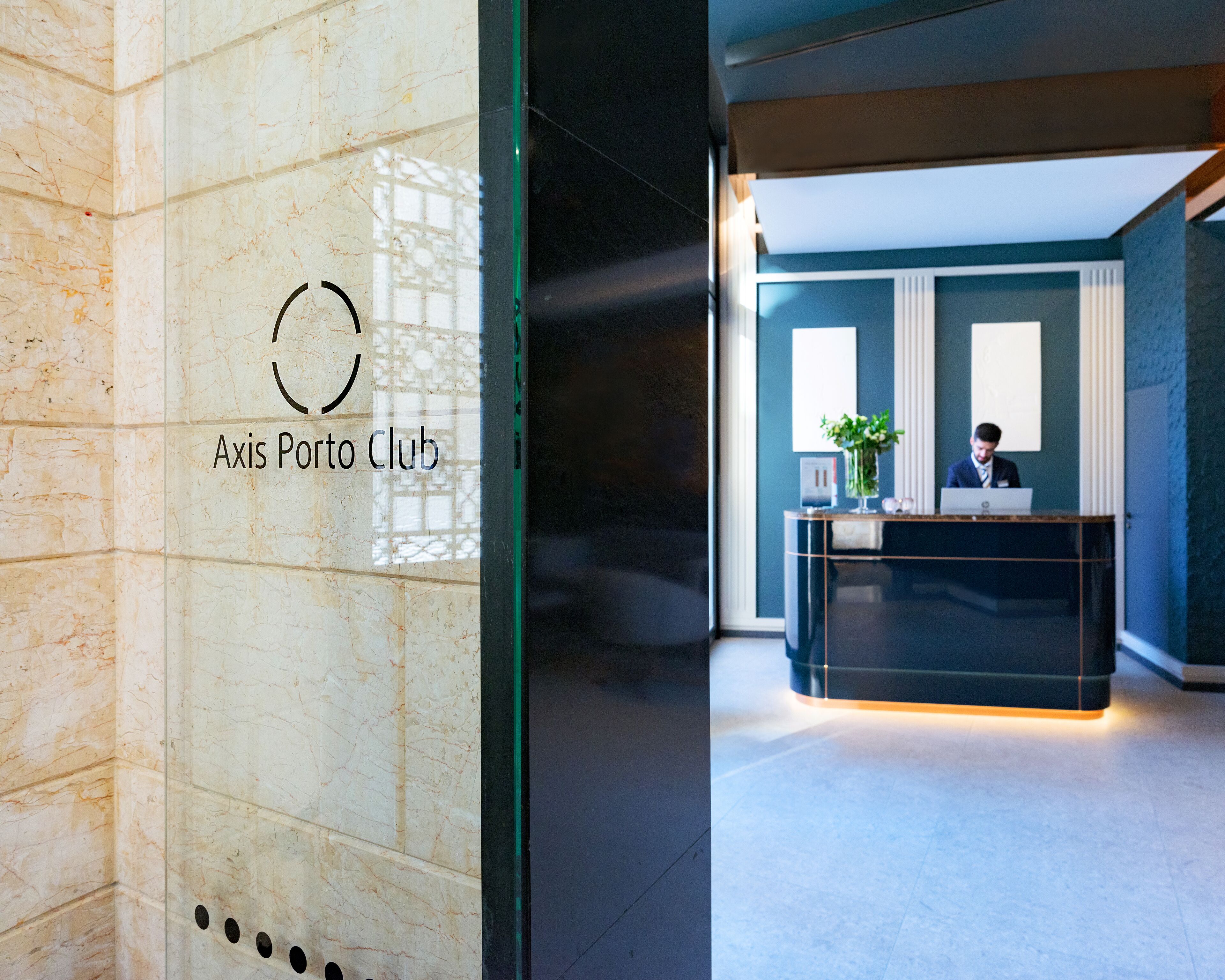 A reception desk with a sign reading "Axis Porto Club" and a man working at the desk.
