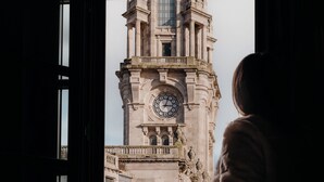 A person standing by a window with a view of a historic building featuring a prominent clock tower. - Axis Porto Club Aliados (Porto)
