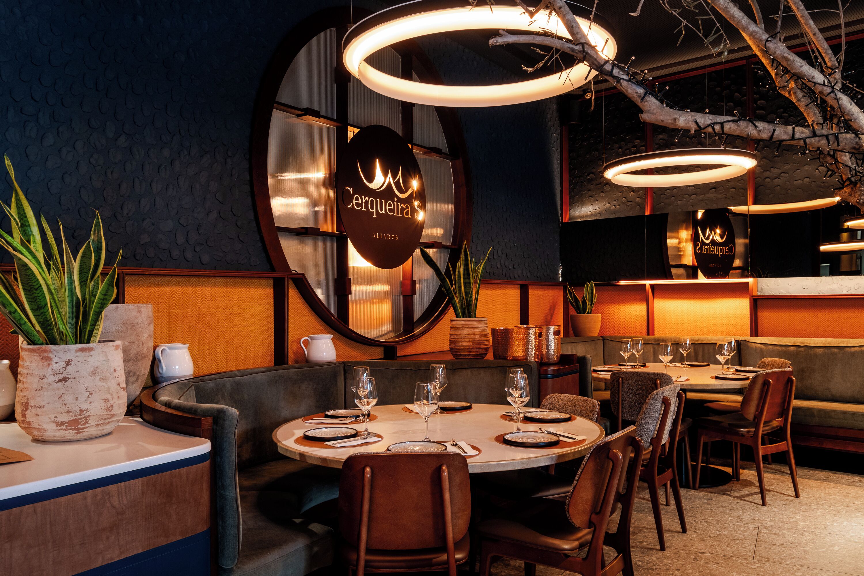 A restaurant interior with round tables, brown leather booths, and modern pendant lighting.