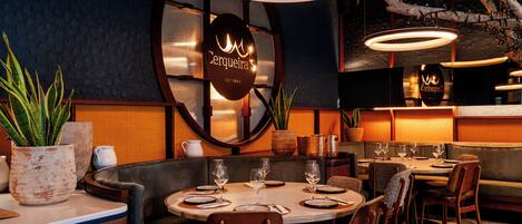 A restaurant interior with round tables, brown leather booths, and modern pendant lighting.