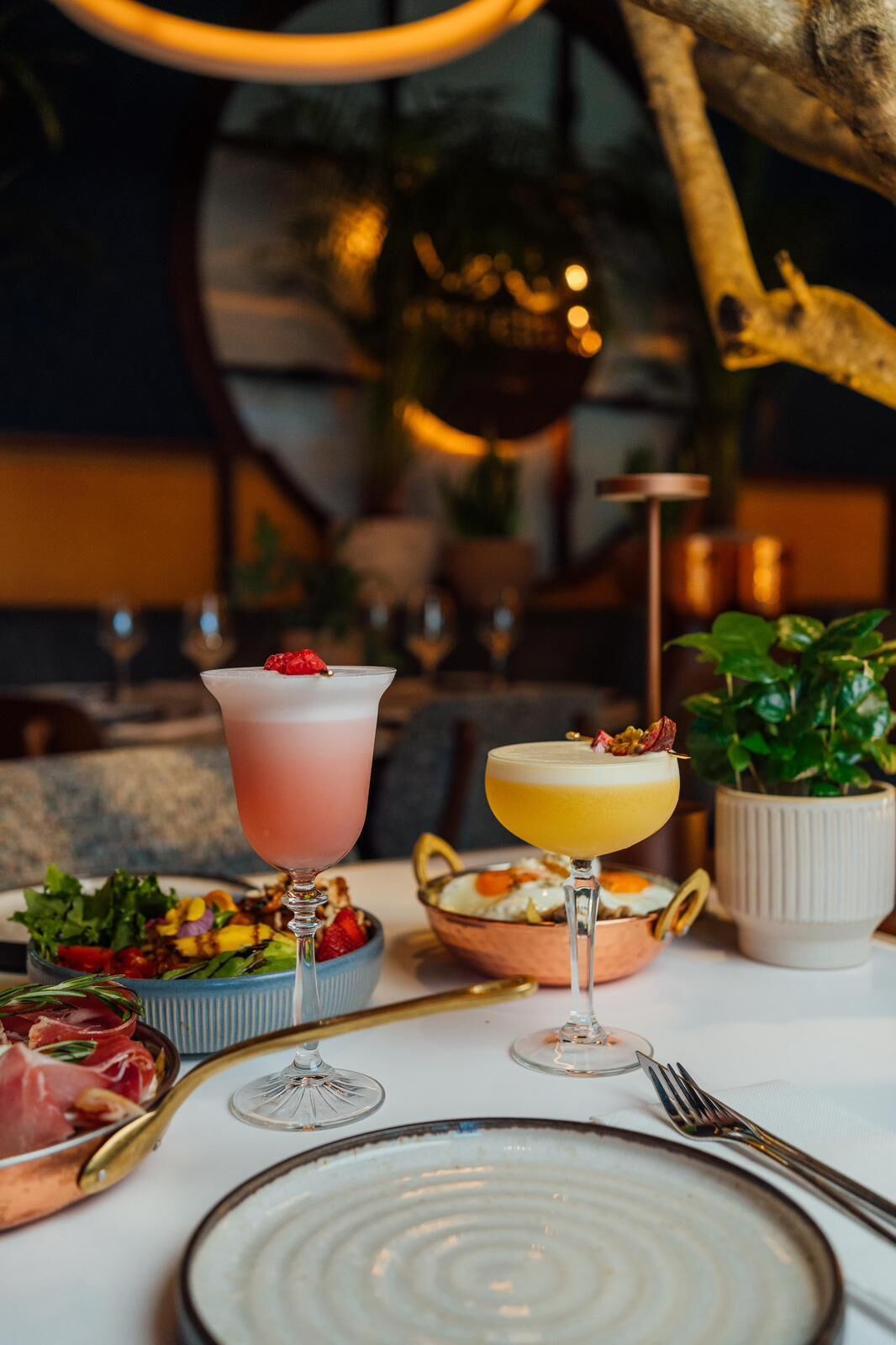 A table set with two drinks, a salad, and a dish of eggs.