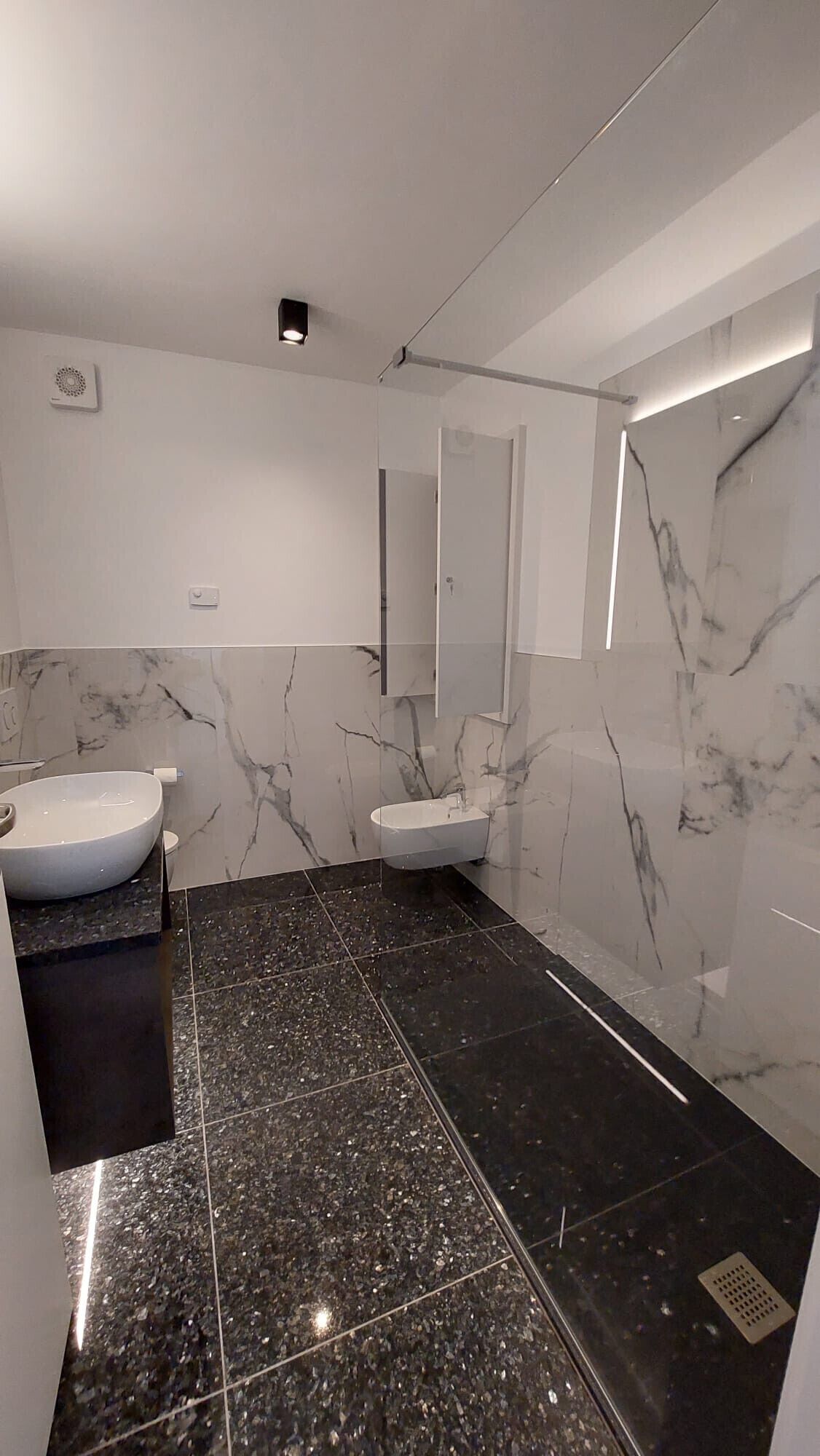 Une salle de bain moderne avec deux lavabos, des murs en marbre et un grand miroir.
