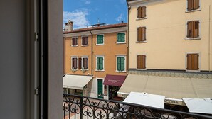 A view from a balcony with a wrought iron railing, overlooking a row of buildings with varying architectural styles and a clear blue sky.