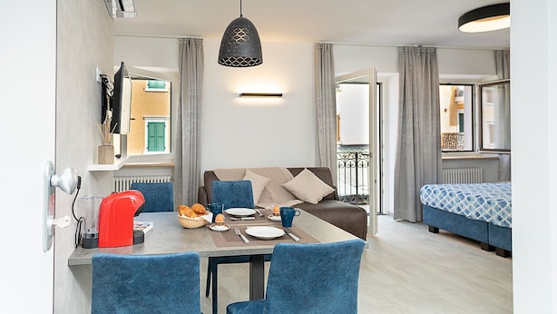 A modern living room with a sofa, a dining table with chairs, and a kitchen area with a red kettle.