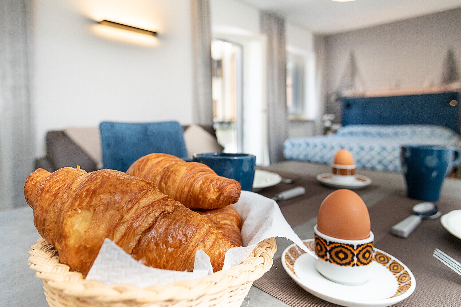 Une table mise pour le petit-déjeuner avec des croissants, une tasse de café et une assiette contenant un œuf.