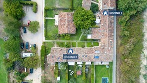 Vista aérea de una zona residencial con dos propiedades señaladas, NOCINO 1 y NOCINO 2, que muestran casas adosadas con tejados de tejas, rodeadas de vegetación y una pequeña carretera.