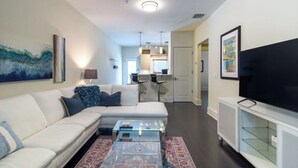A modern living room with a sectional sofa, a glass coffee table, a flat-screen TV, and artwork on the walls. - Walk The Downtown Village of Winter Park!!! (Winter Park)