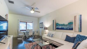 A living room with a white sofa, a glass coffee table, a ceiling fan, and artwork on the walls. - Walk The Downtown Village of Winter Park!!! (Winter Park)
