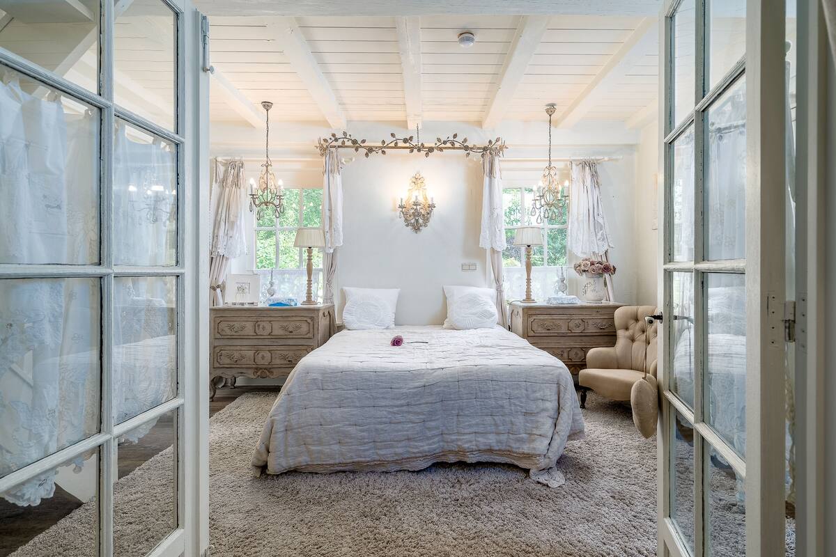 Een slaapkamer met een groot bed, een hemelbed, een kroonluchter en uitzicht door het open raam.