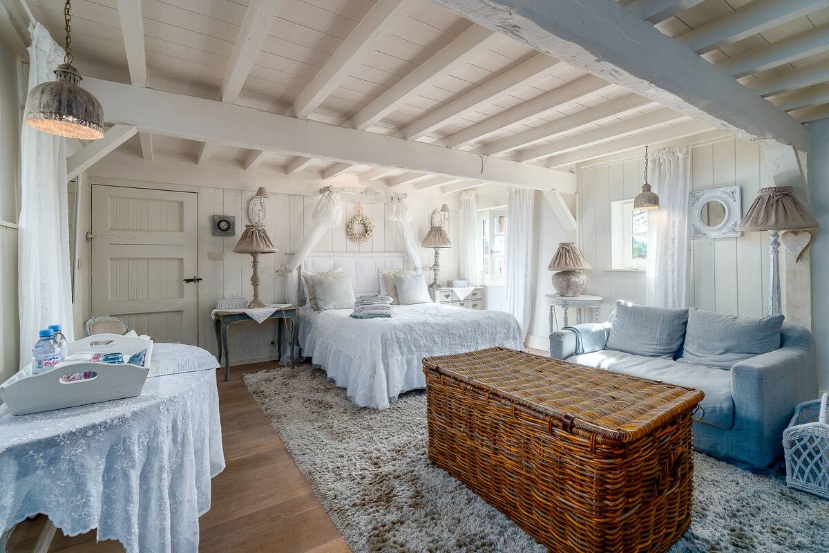 Een gezellige slaapkamer met een bed, nachtkastjes, een rieten kist, een bank en een bureau met een laptop.