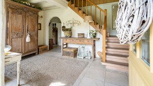 Une pièce spacieuse avec un escalier en bois, une grande armoire en bois, une console agrémentée d’objets décoratifs et un tapis douillet.