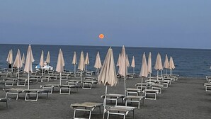 A beach with rows of sun loungers and umbrellas, a clear sky, and the ocean in the background.